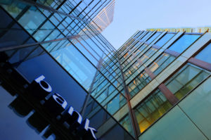 Bank corporate finance building seen from below. The sign "bank" visible close. Sky reflecting in the glass facad