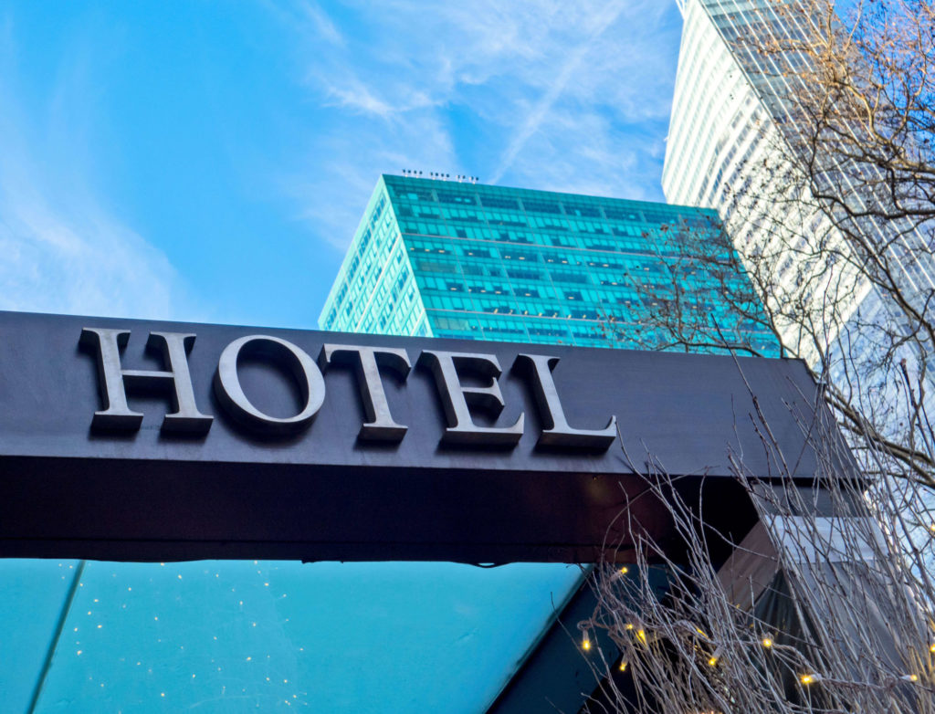 Hotel entrance in daytime seen from below. The sign "hotel" visible close. Sky and adjacent building in the background.